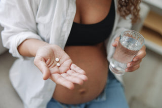 pregnant woman holding two vitamins and glass of water